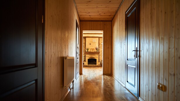 Ein Holzboden führt zu einem Kamin mit steinernen Verkleidungen, flankiert von Holztüren und einem Heizkörper.