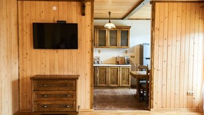 Ein Holzinnenraum mit an der Wand montiertem Fernseher, Holzschränken, einer Essecke mit einem Stuhl und einer Küchenzeile mit Kühlschrank.