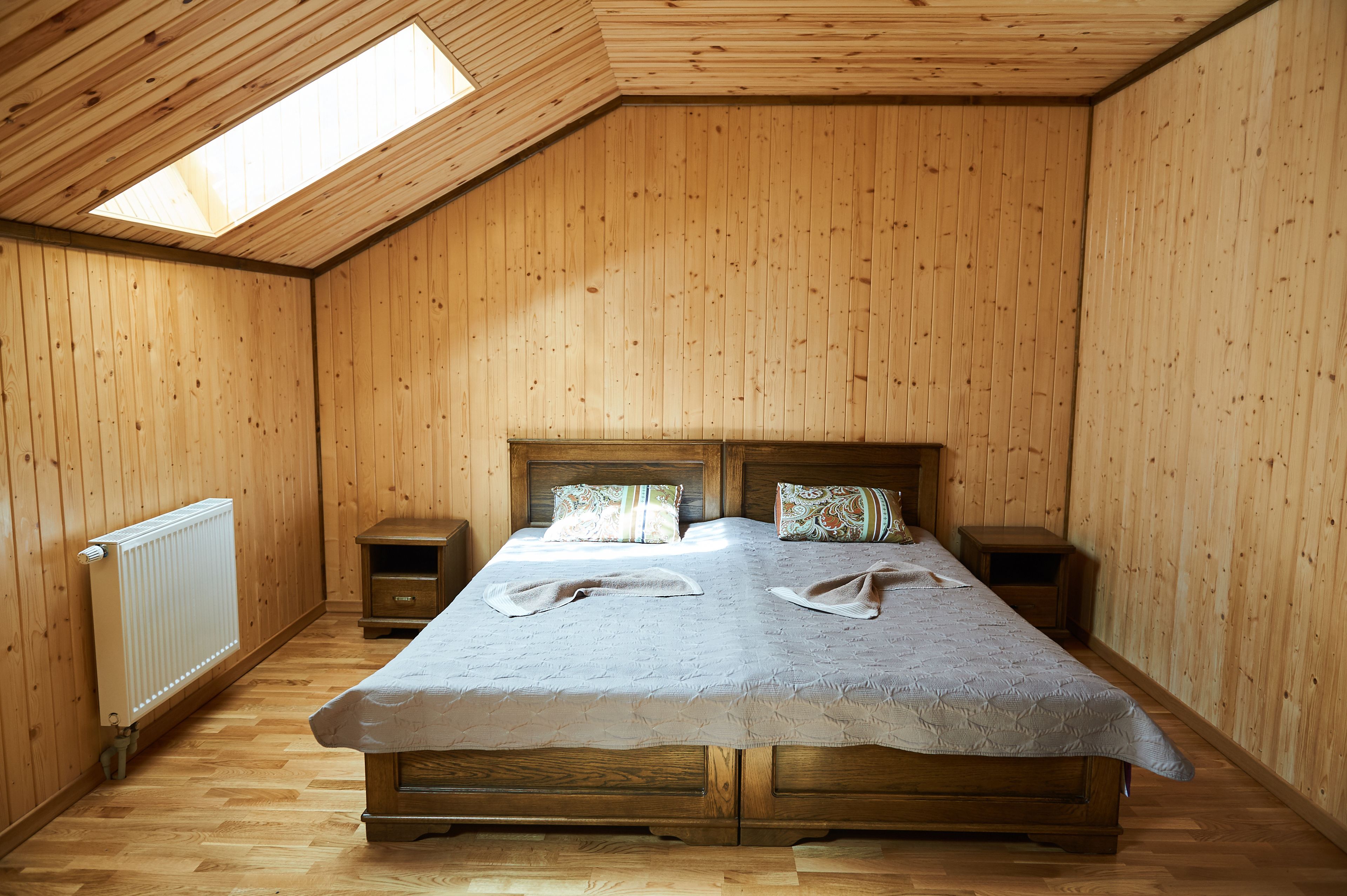 Une chambre aux murs lambrissés, avec un grand lit, deux tables de chevet et une lucarne.