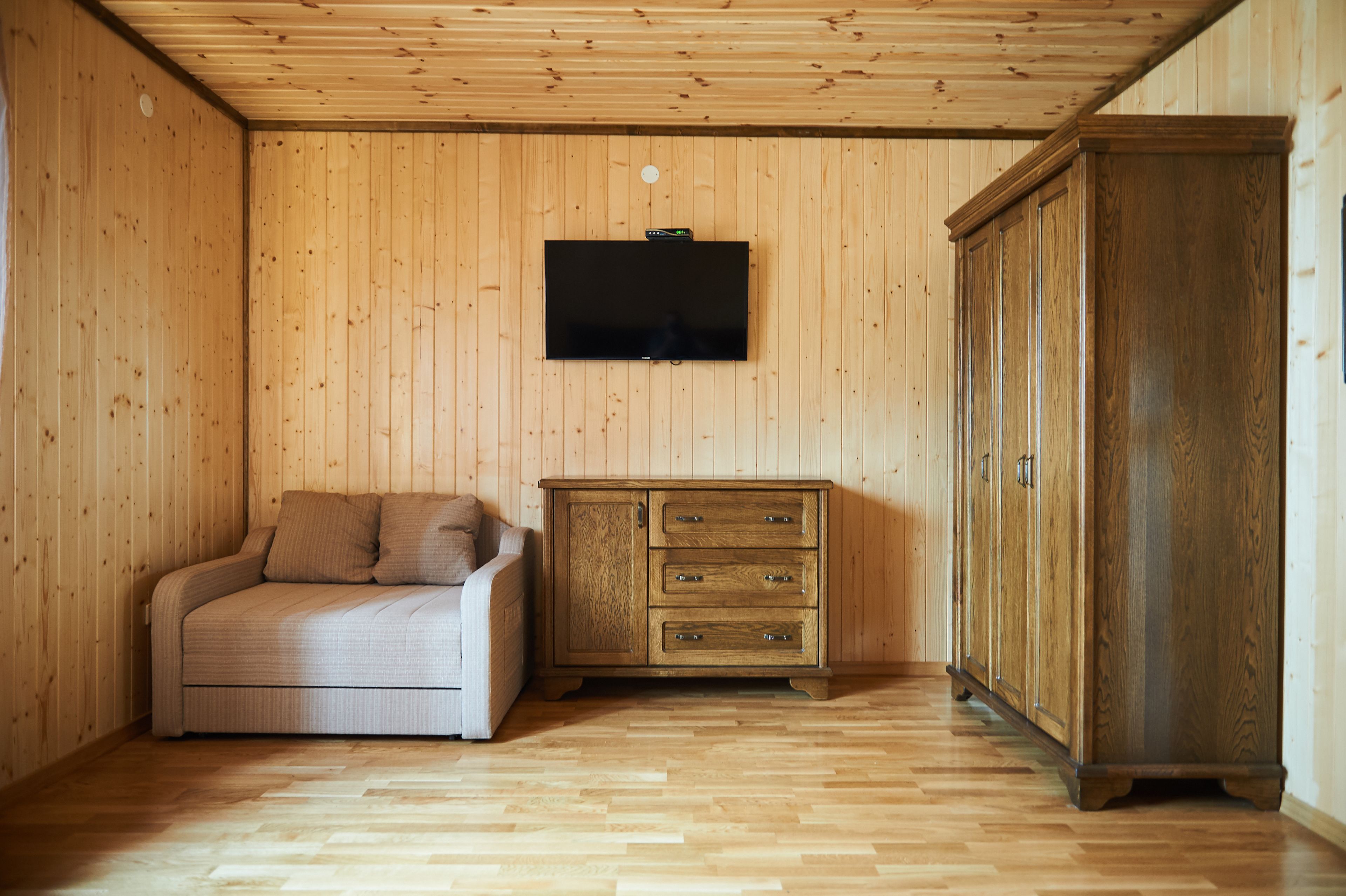 A room with wooden walls and floor, a flat-screen TV mounted on the wall, a sofa, and a wooden cabinet.