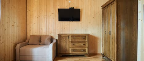 A room with wooden walls and floor, a flat-screen TV mounted on the wall, a sofa, and a wooden cabinet.