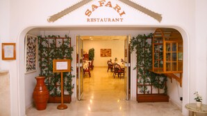 La entrada a un restaurante llamado 'Safari Restaurant', con piso de baldosas, muebles de madera y plantas en macetas.