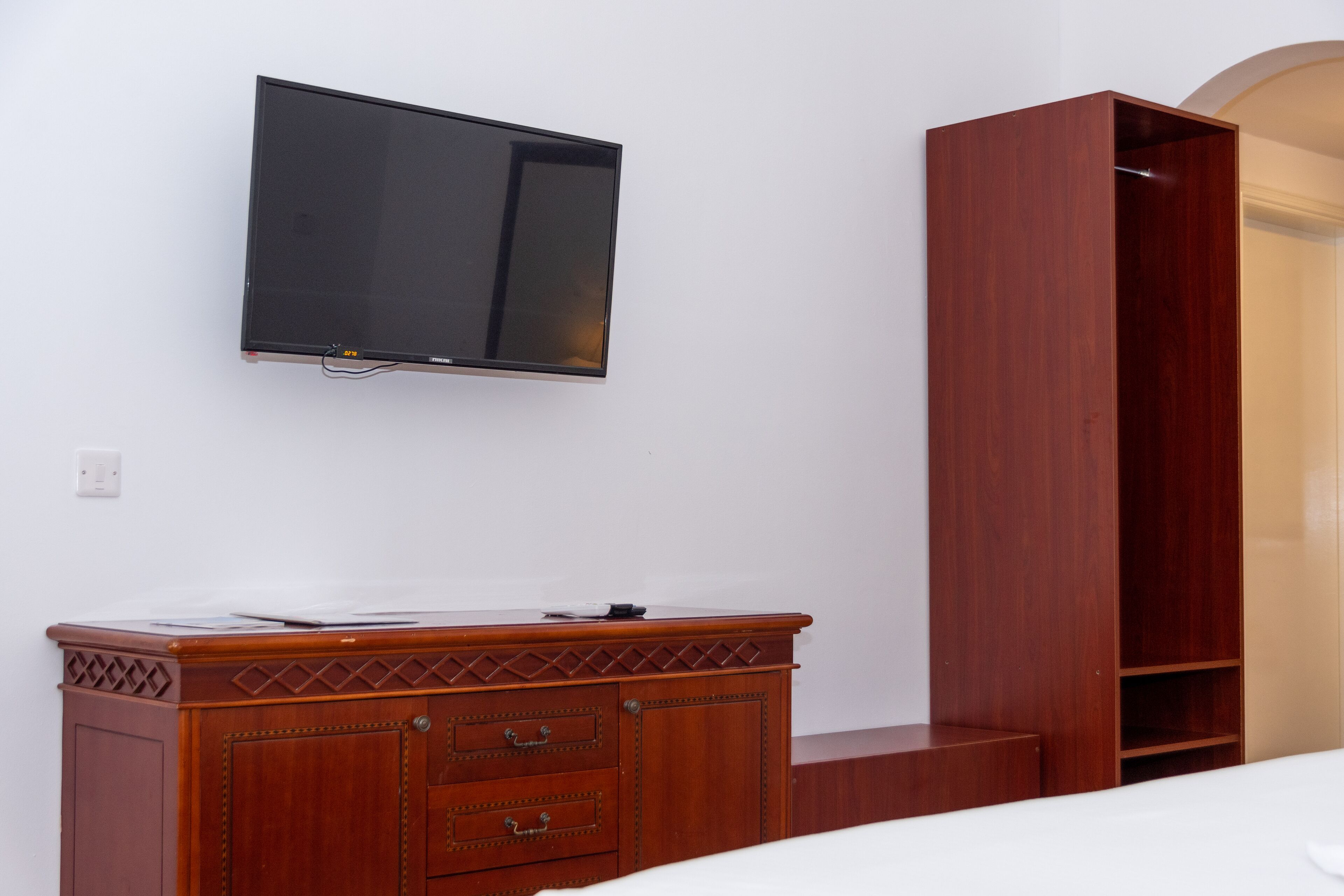 A bedroom with a wooden dresser, a television mounted on the wall, and a wardrobe.