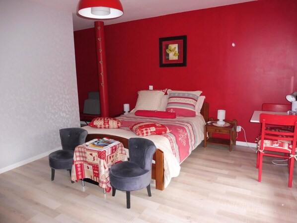 Un dormitorio con una cama, dos sillas, una mesa y una pared roja.