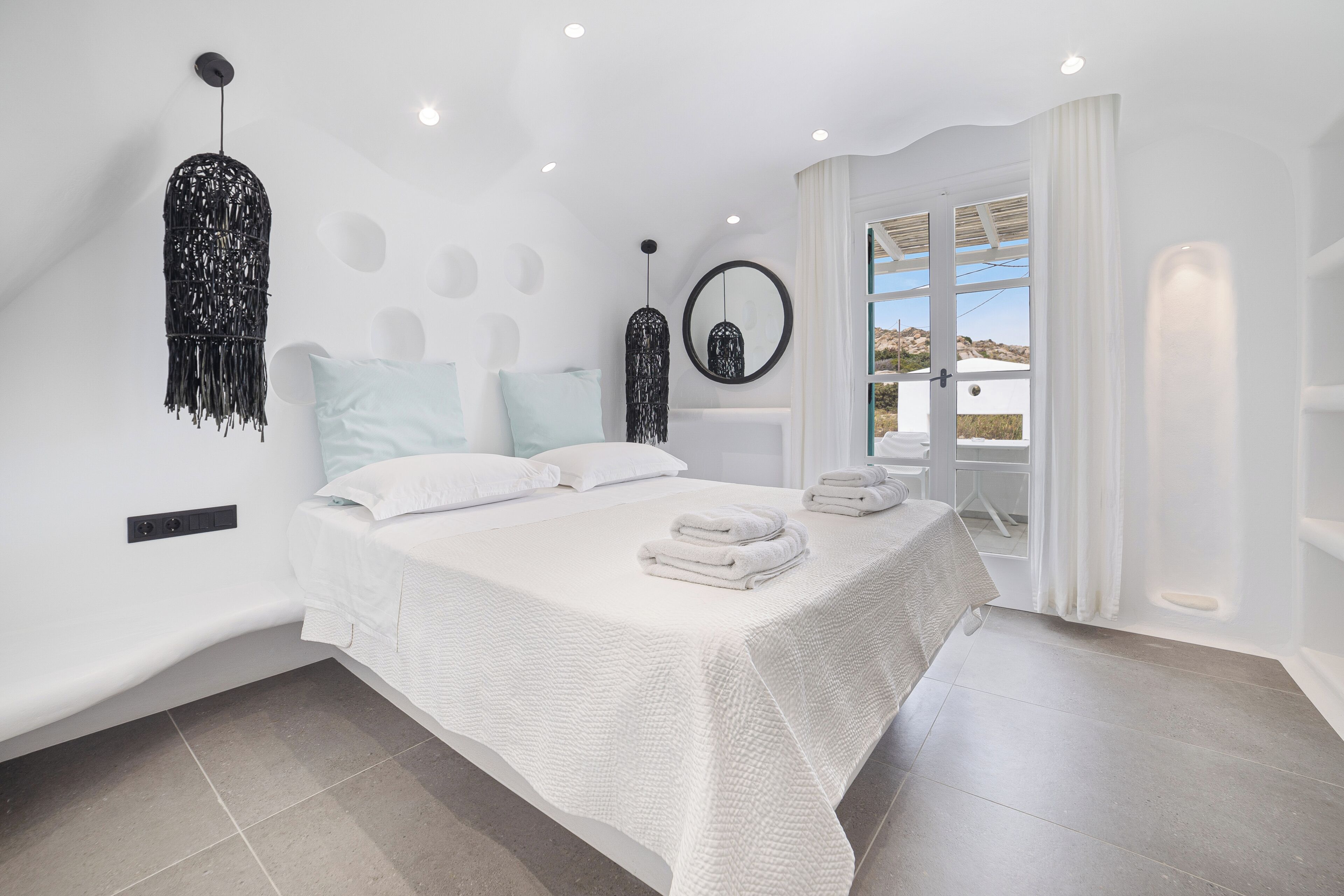 A modern bedroom with a large bed, a hanging light fixture, and a view through a glass door.