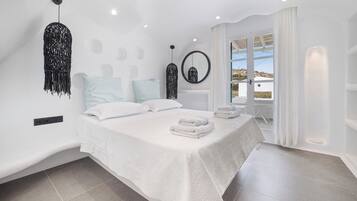 A modern bedroom with a large bed, a hanging light fixture, and a view through a glass door.