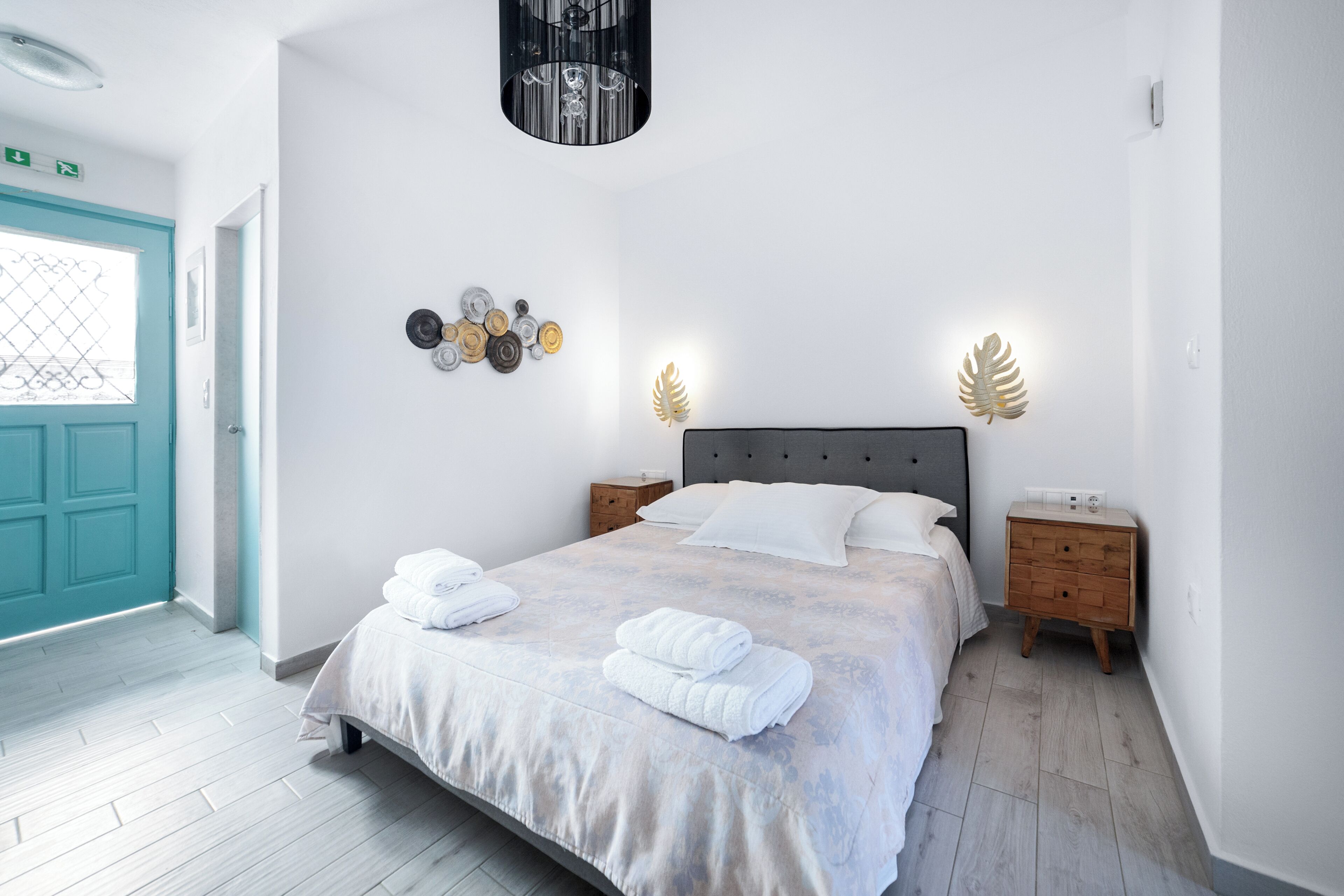 Un dormitorio con cama, mesitas de noche, una lámpara de pared y una puerta.