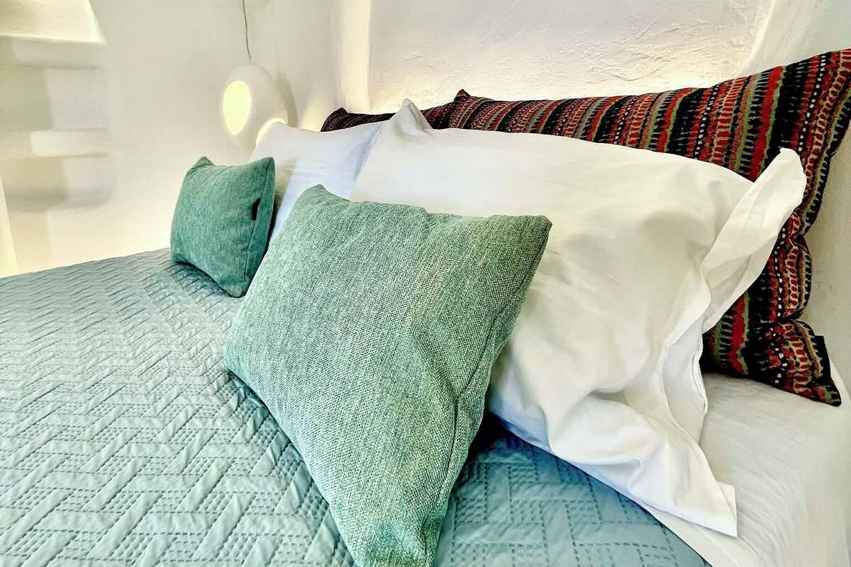 A bed with a quilted blue cover, a white pillow, and two green pillows.