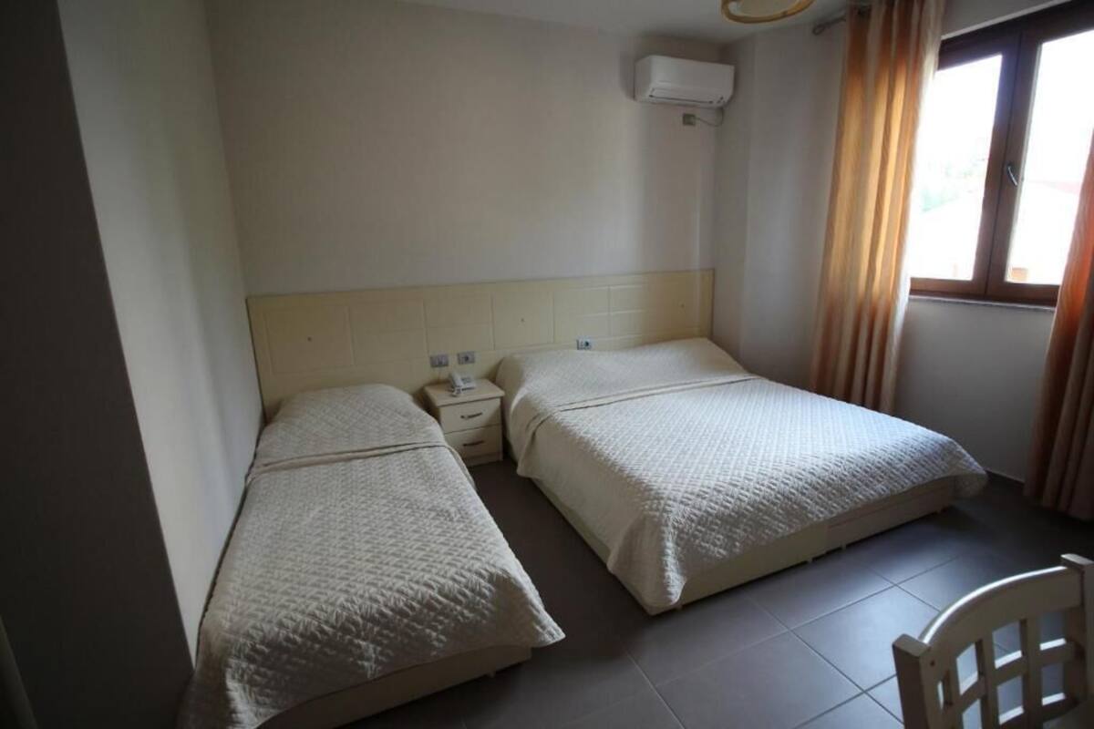 A room with two beds, a nightstand, a chair, and a window with curtains.