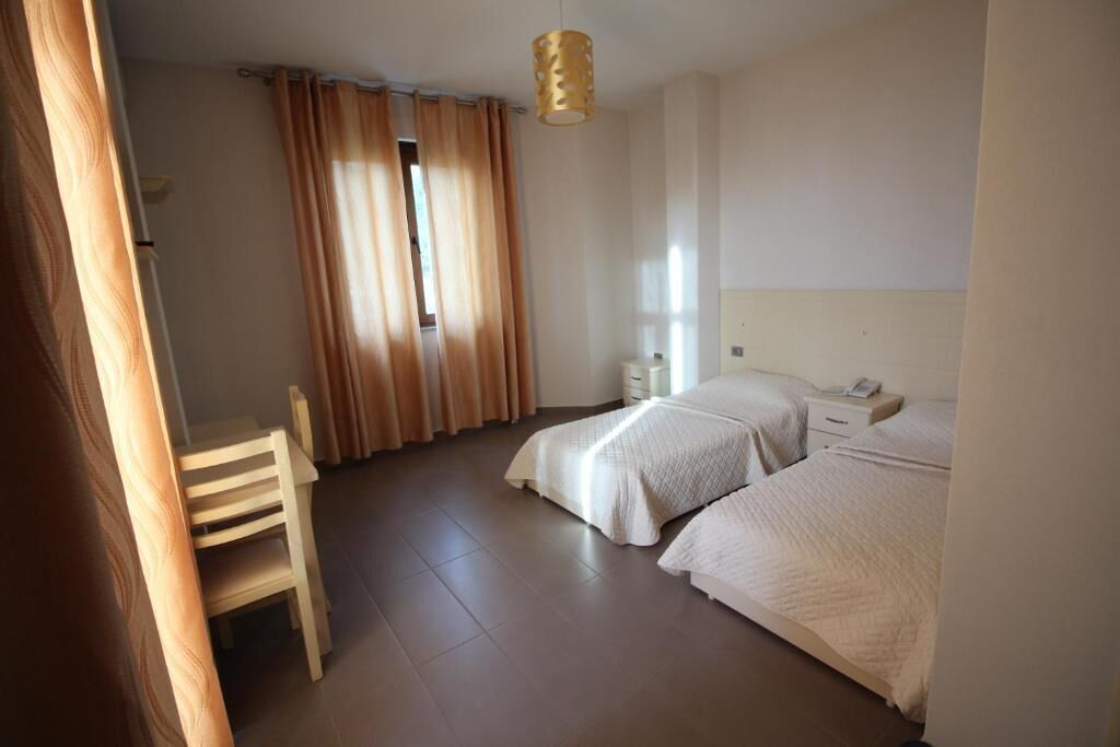 A bedroom with two beds, a chair, a bedside table, and a hanging light fixture.