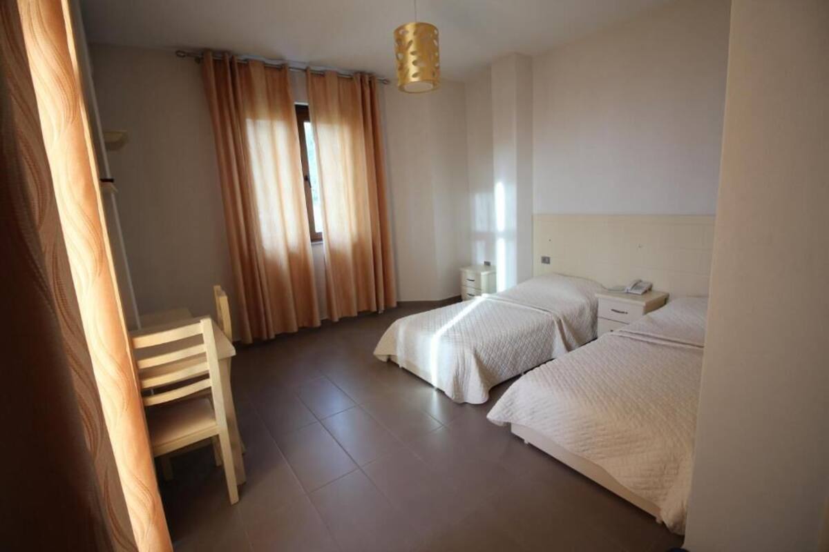 A bedroom with two beds, a chair, a bedside table, and a hanging light fixture.