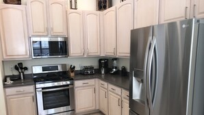 A kitchen with white cabinets, stainless steel appliances including a microwave, stove, oven, and refrigerator. - Dolphin's Retreat Near Disney (Kissimmee)
