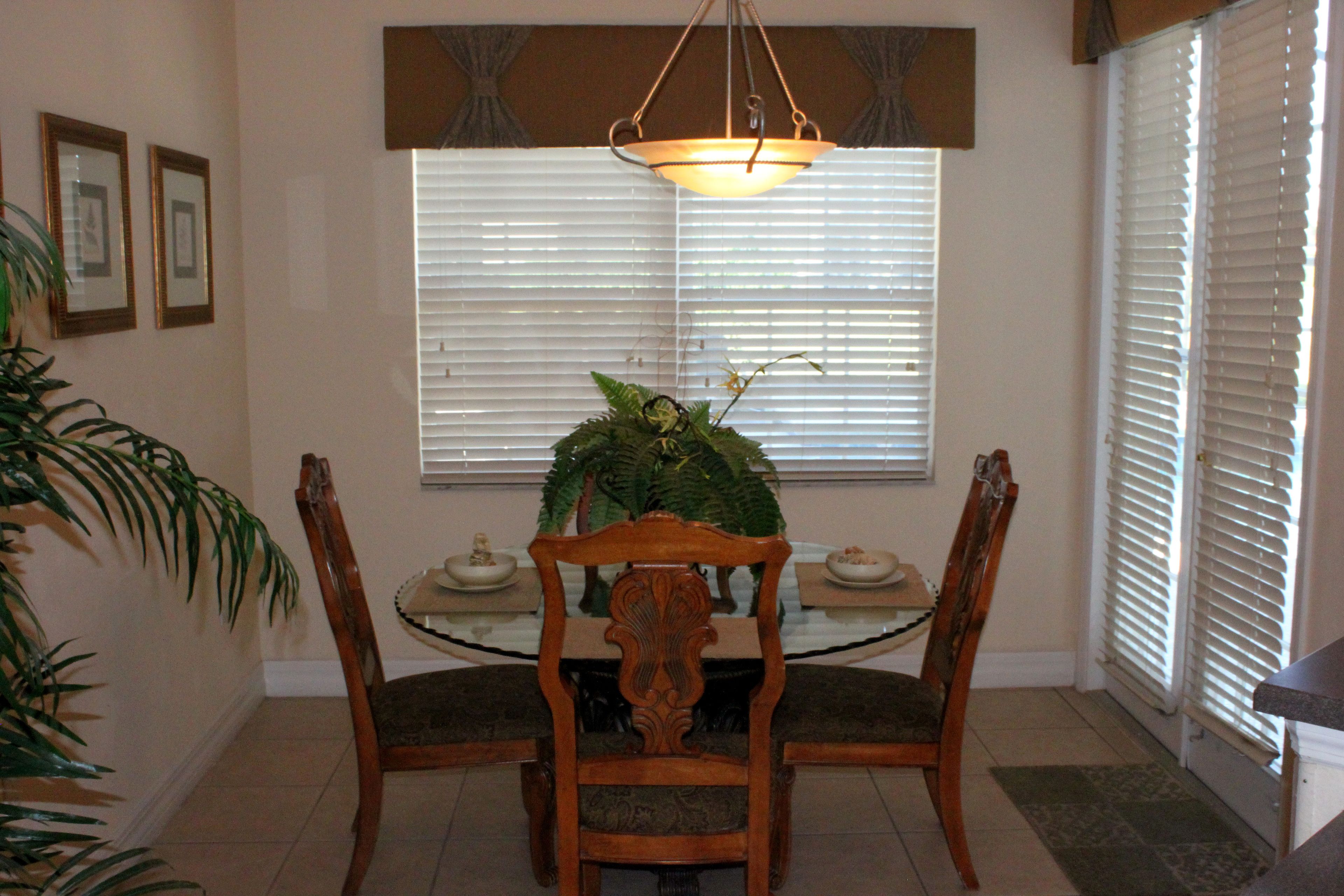 A dining area with a glass table, wooden chairs, a central plant, and a hanging light fixture.