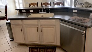 A kitchen with a built-in sink, white cabinets, a stainless steel dishwasher, and a window with blinds. - Dolphin's Retreat Near Disney (Kissimmee)