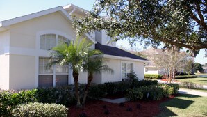 A two-story house with a white exterior, a dark roof, and a well-maintained front yard with red mulch, various shrubs, and a palm tree. - Dolphin's Retreat Near Disney (Kissimmee)
