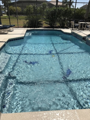Une piscine aux eaux cristallines, bordée de carreaux, entourée d’une terrasse aménagée avec des chaises et des tables.