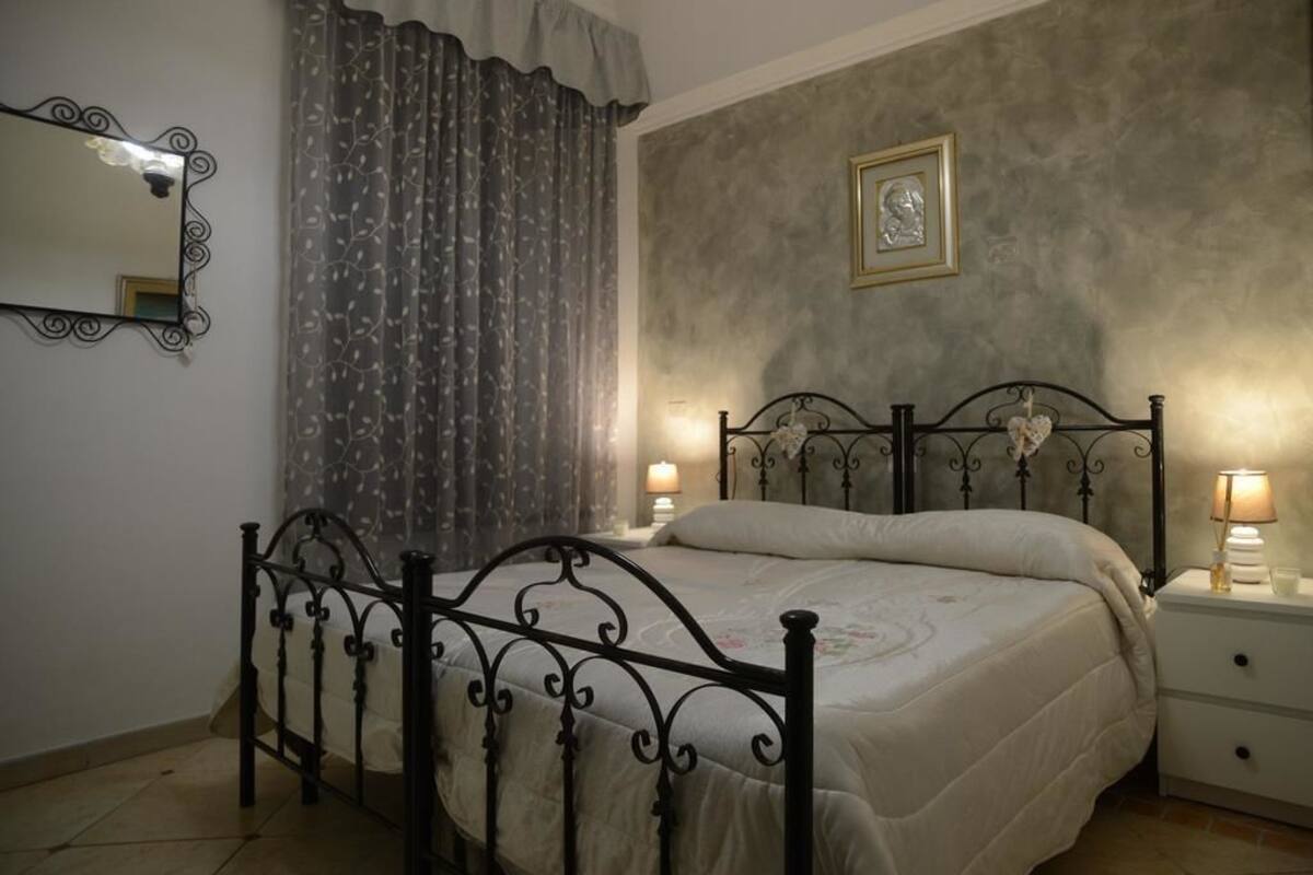 A bedroom with a bed, a nightstand, a mirror, and a wall with a framed picture.