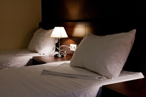 Ett hotellrum med två sängar, ett nattduksbord med en lampa och en sänggavel i trä.