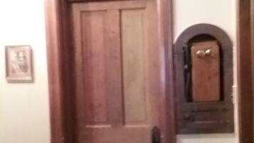 A wooden door with a small window above it, a framed picture on the wall, and a small shelf with a clock.