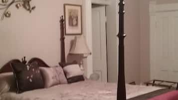 Un dormitorio con una cama con dosel, un ventilador de techo, una lámpara y una puerta que da a otra habitación.