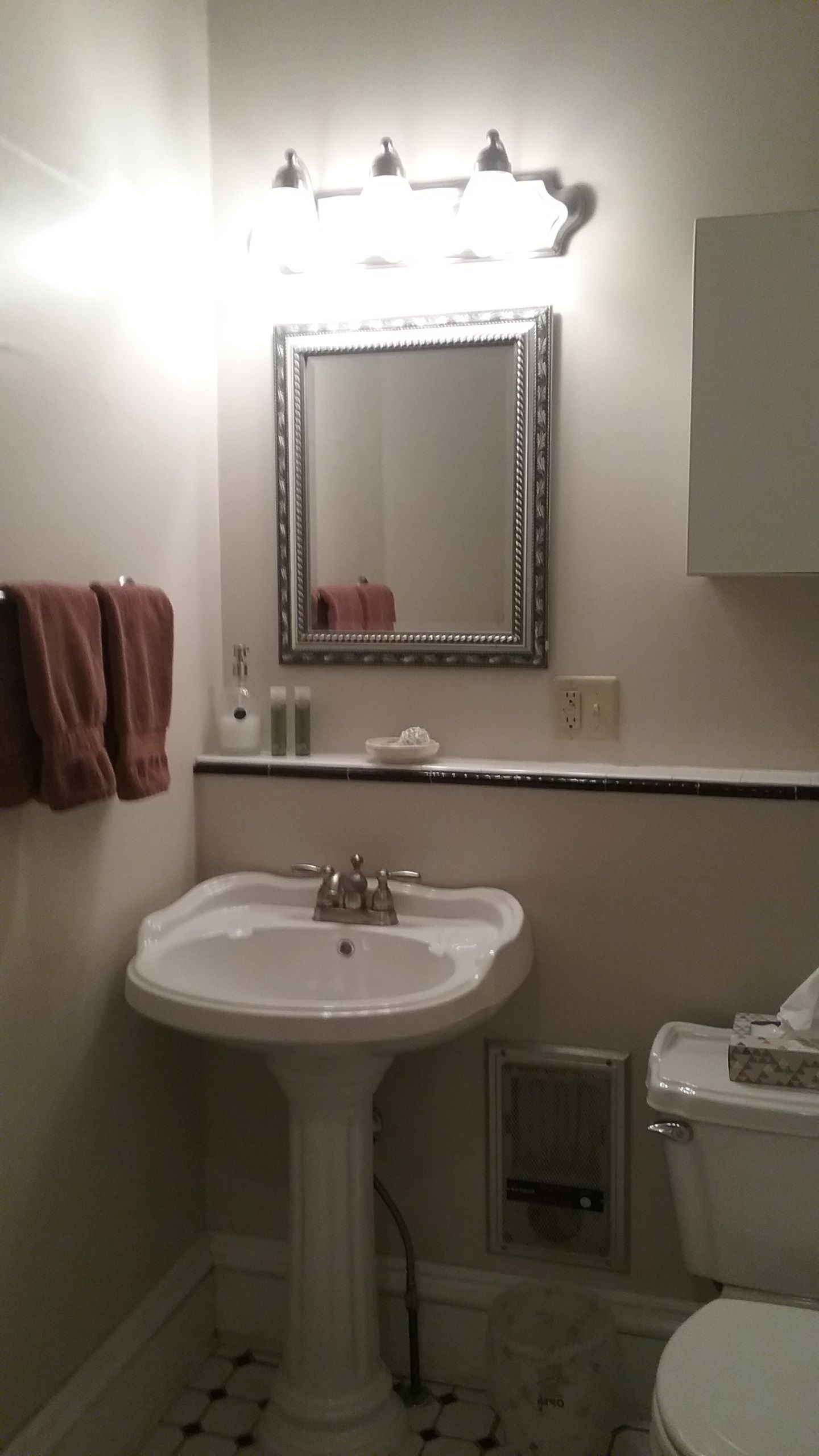 Uma casa de banho com uma pia branca, um espelho iluminado, um porta-toalhas com toalhas e uma sanita.