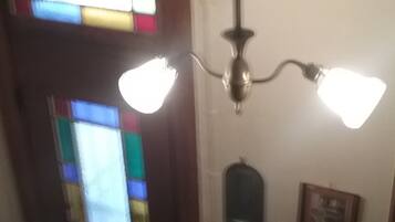 Un pasillo con una puerta de vitral, una lámpara de pared y un pequeño cuadro enmarcado.