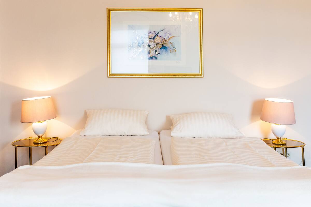 Un lit double avec deux tables de chevet, chacune équipée d’une lampe, et une œuvre d’art encadrée au-dessus du lit.