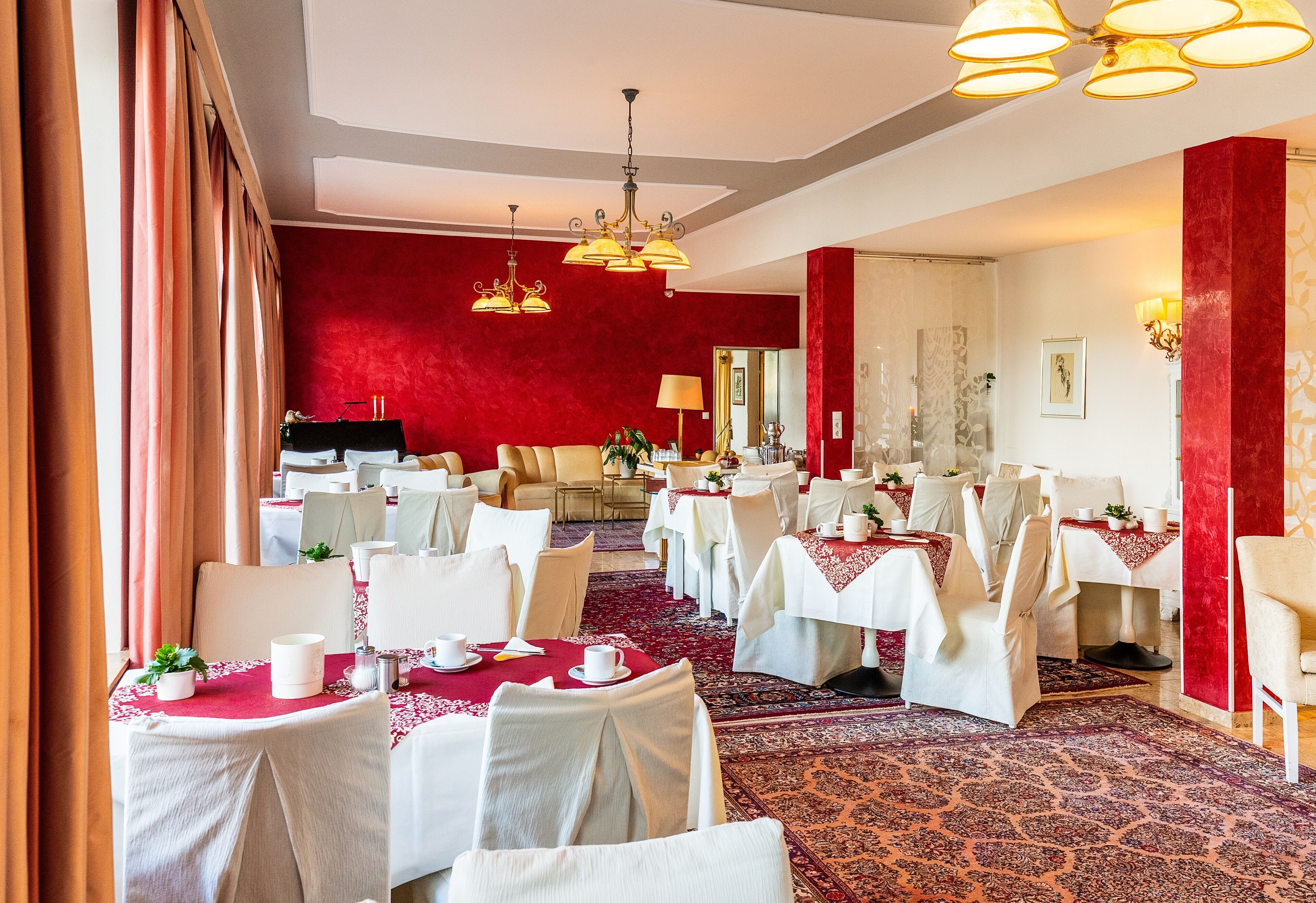 A dining area with tables set for service, a red accent wall, and a chandelier.