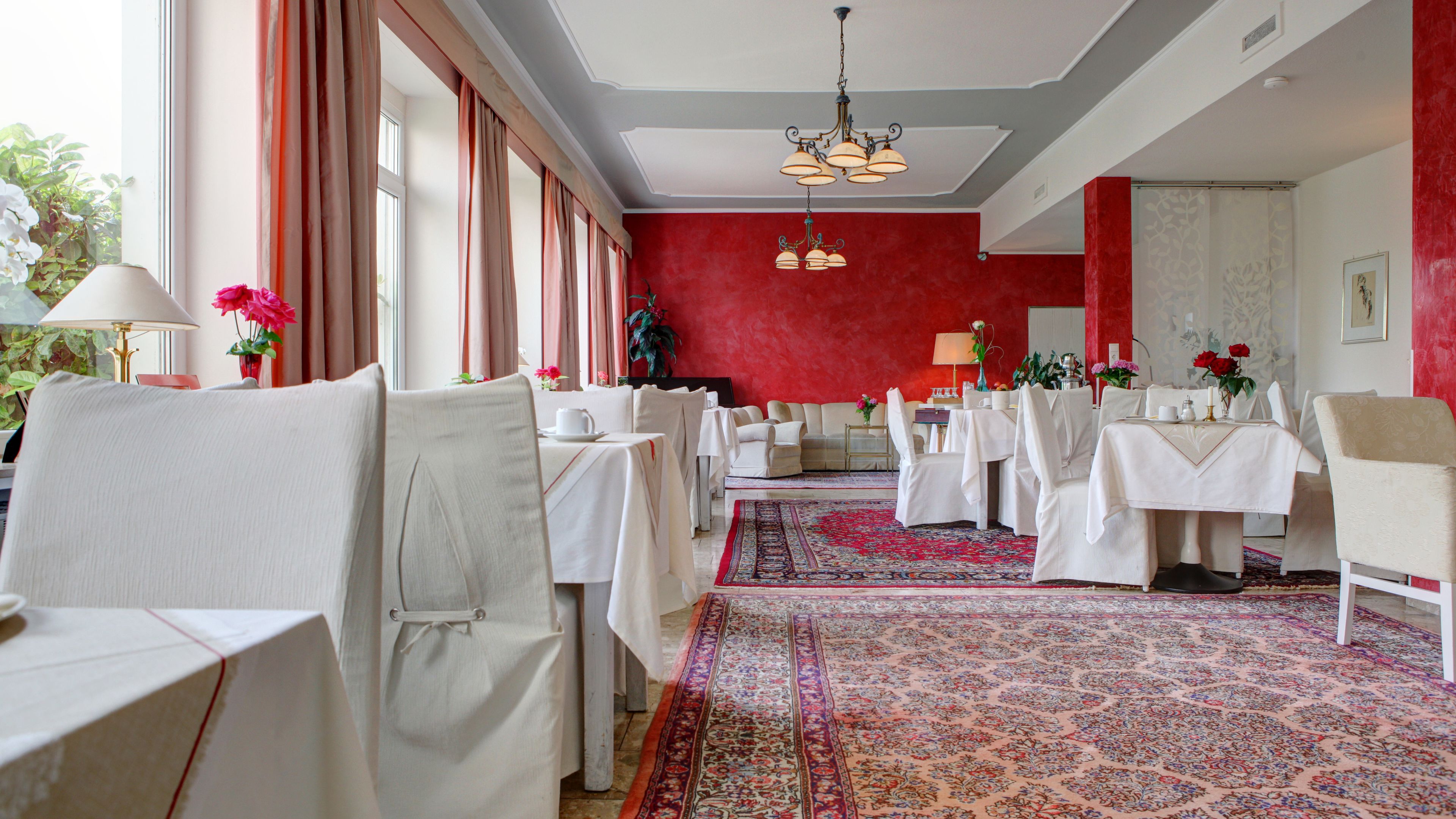 Un comedor con mesas dispuestas para el servicio, una alfombra estampada y una pared de acento roja.