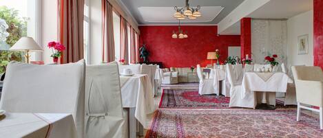 Un comedor con mesas dispuestas para el servicio, una alfombra estampada y una pared de acento roja.