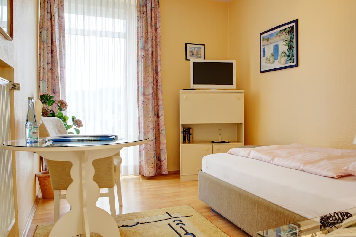 Une chambre d’hôtel comprenant un lit, un bureau avec un ordinateur, une chaise, une lampe, un téléphone et une fenêtre avec des rideaux.