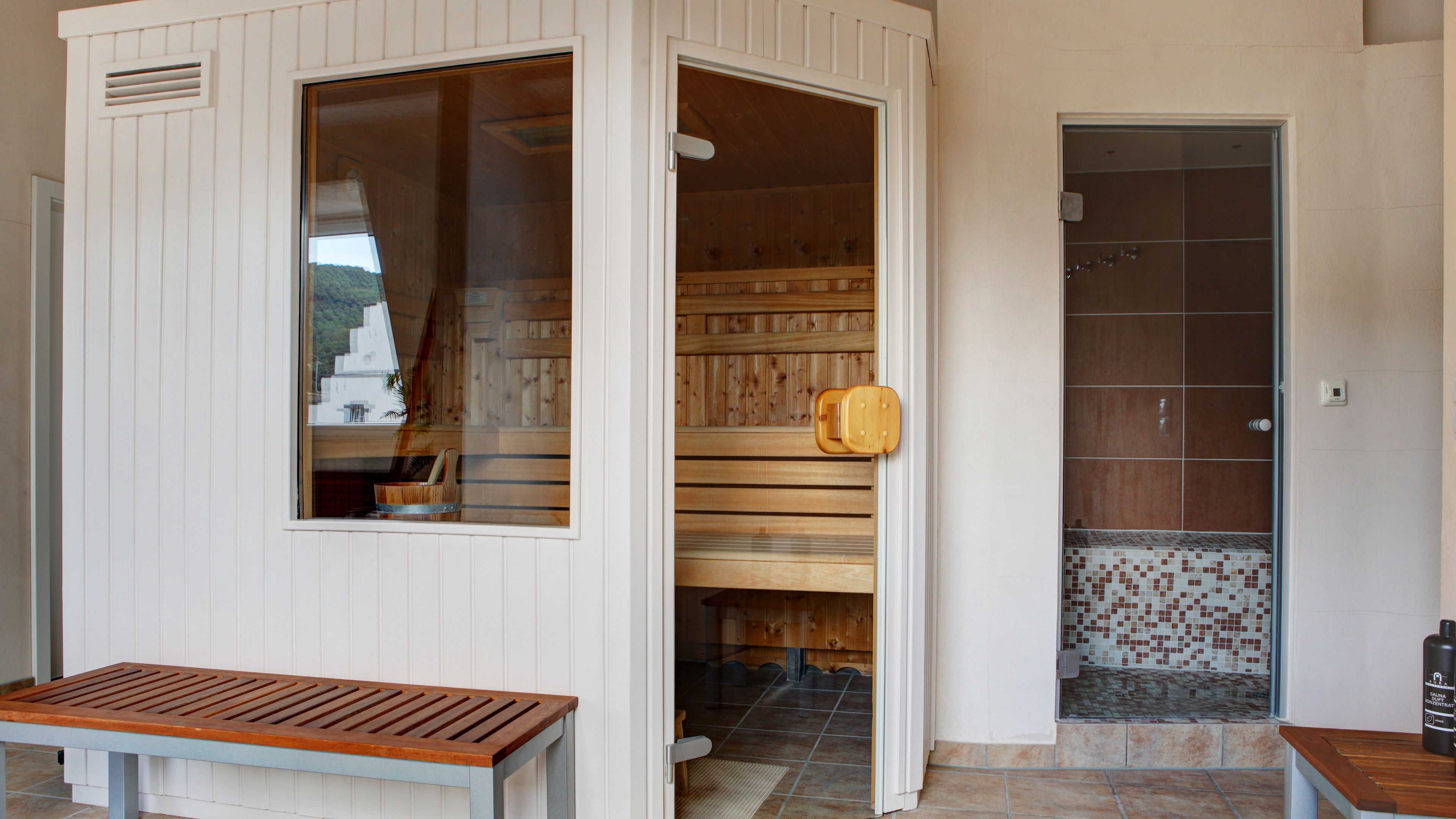 Una stanza sauna con una panca, panche di legno all'interno e un angolo doccia rivestito in piastrelle.