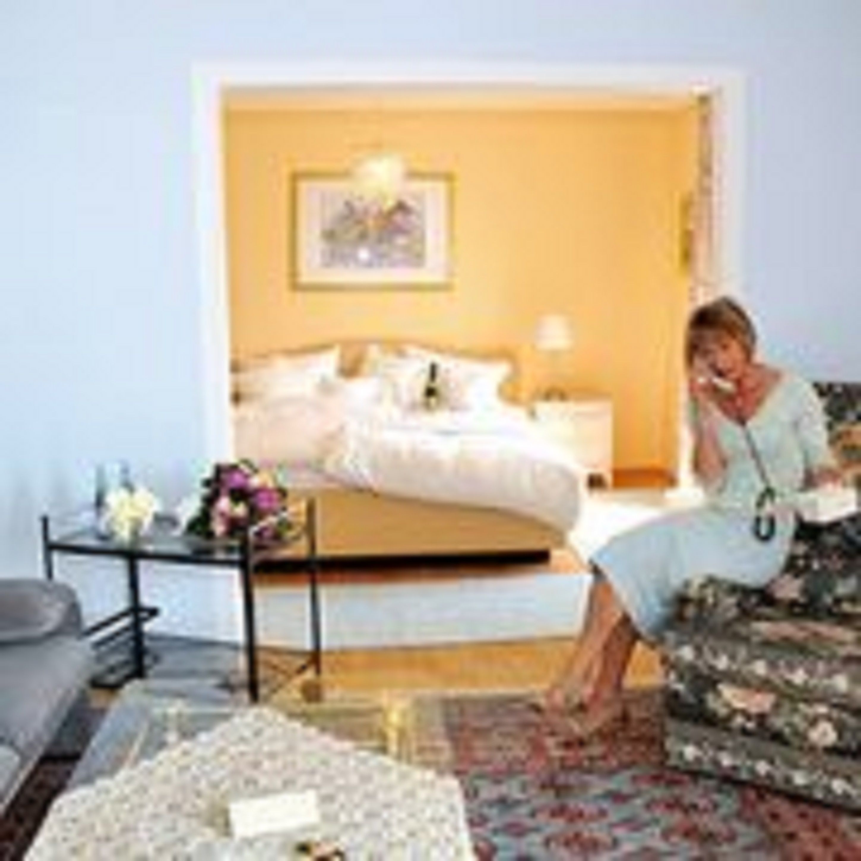 A hotel room with a bed, a bedside table with a lamp, a chair, and a small table with a vase of flowers.