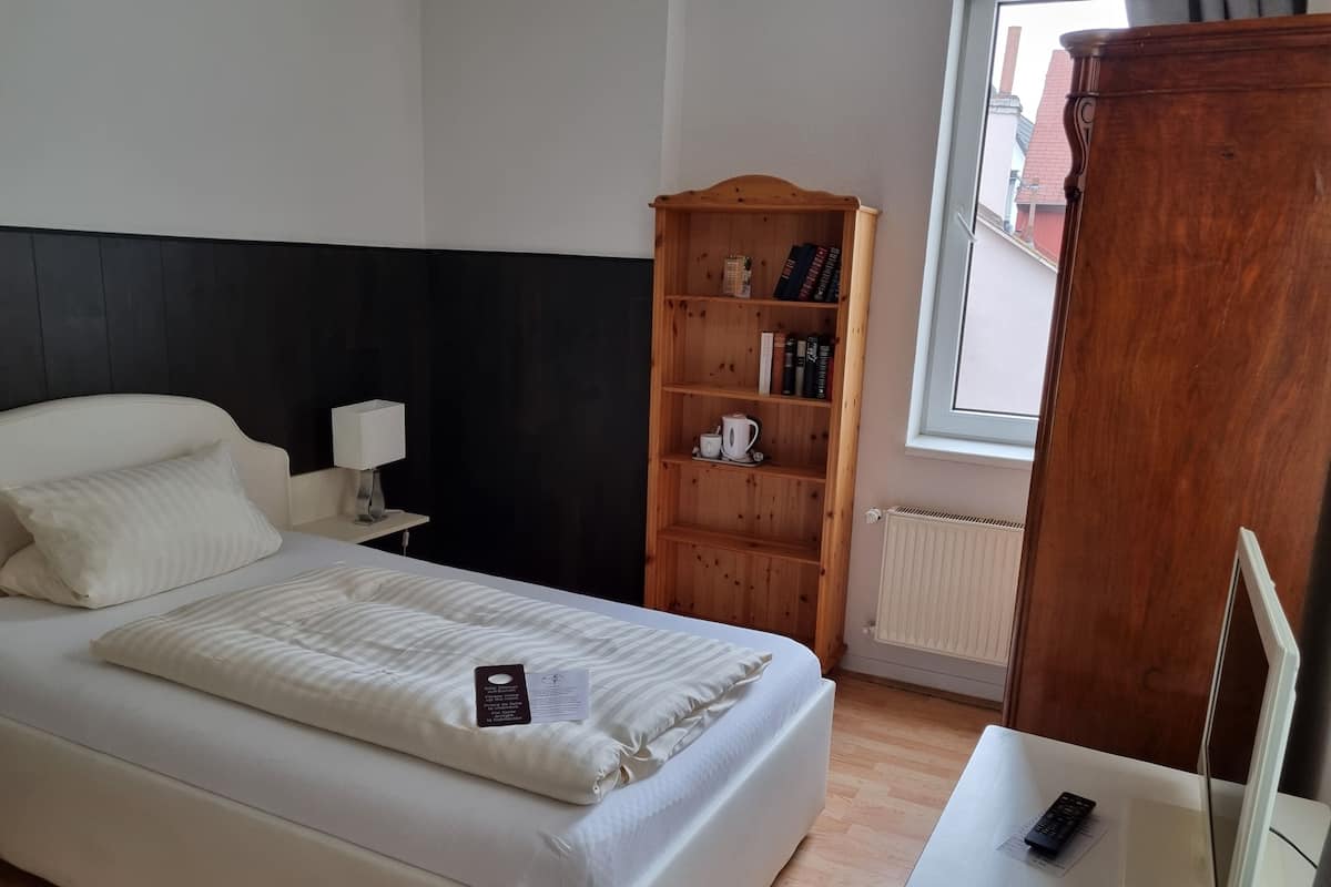 Une chambre d’hôtel bien aménagée, avec un grand lit, une bibliothèque en bois, une table de chevet et une fenêtre donnant sur l’extérieur.