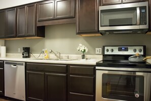 A kitchen with dark wooden cabinets, a stainless steel microwave, a Whirlpool oven, a coffee maker, and a vase with flowers. - Modern Upscale Private Room (Raleigh)