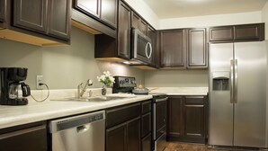 A modern kitchen with dark wood cabinets, stainless steel appliances, and a marble countertop. - Modern Upscale Private Room (Raleigh)