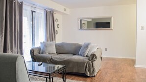 A living room with a sofa, a glass coffee table, and a patterned rug. - Modern Upscale Private Room (Raleigh)