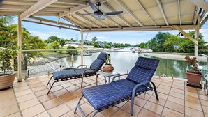 A covered outdoor seating area with two lounge chairs, a table, and a ceiling fan.