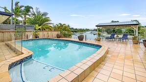 A swimming pool with tiled edges, lounge chairs, and potted plants.