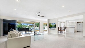 A spacious living area with a white sofa, glass coffee table, and a ceiling fan.