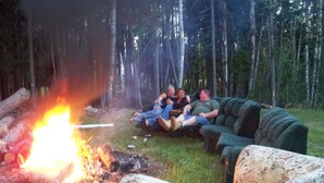 En grupp människor som kopplar av på en soffa nära en lägereld i ett skogsområde.