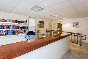 Zona de recepción con un mostrador de madera, estantes con bolsas, una mesita y una escalera.
