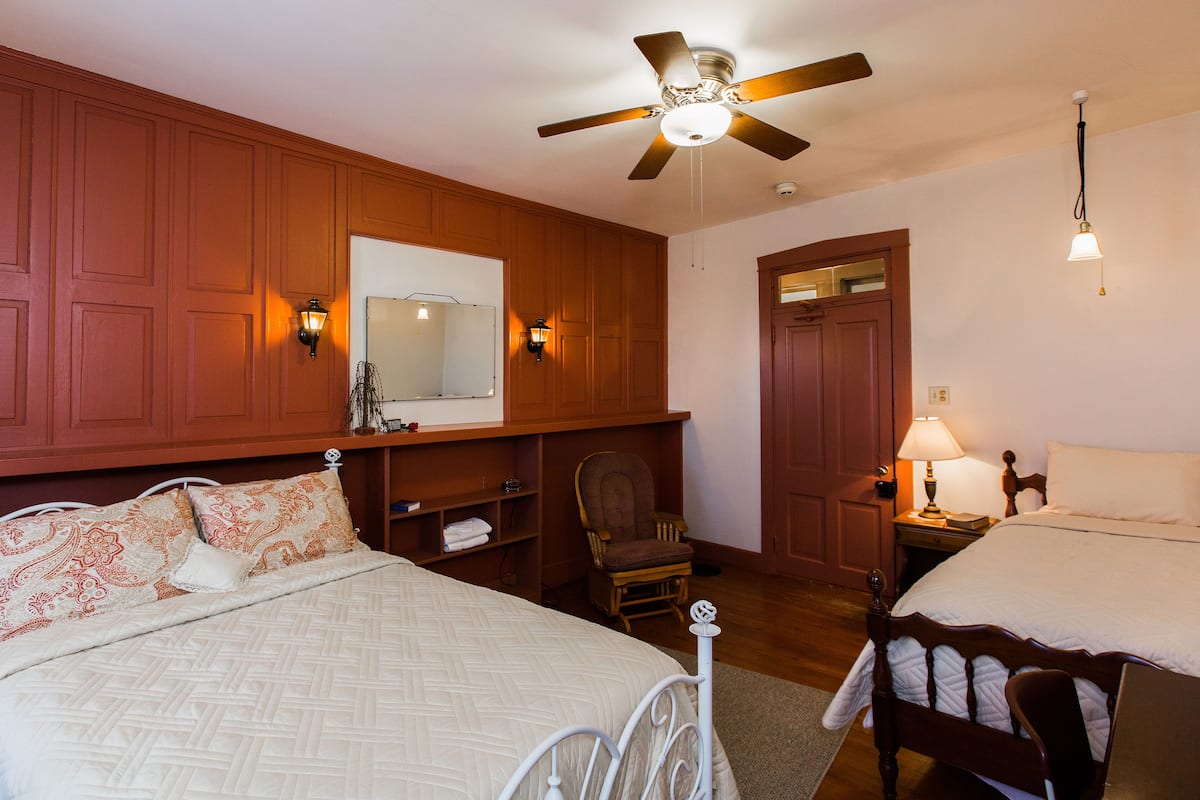 Une chambre à coucher comprenant un lit, une chaise, une table de chevet, un ventilateur de plafond et un miroir.