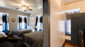 Une chambre d’hôtel avec deux lits, un bureau, une chaise, un ventilateur de plafond et une fenêtre avec des rideaux.