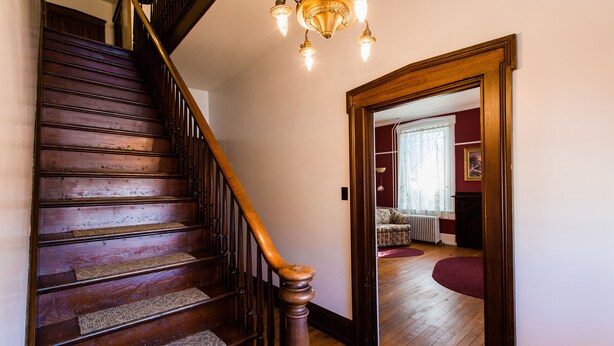 Un escalier en bois avec une rampe, des marches recouvertes de moquette et un lustre au-dessus.