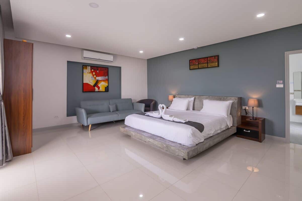 Quarto moderno com uma cama grande, um sofá cinzento e obras de arte nas paredes.