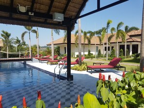 A pool area with red lounge chairs, a thatched roof, and palm trees. - Tamara Resort Bangsary (Sattahip)