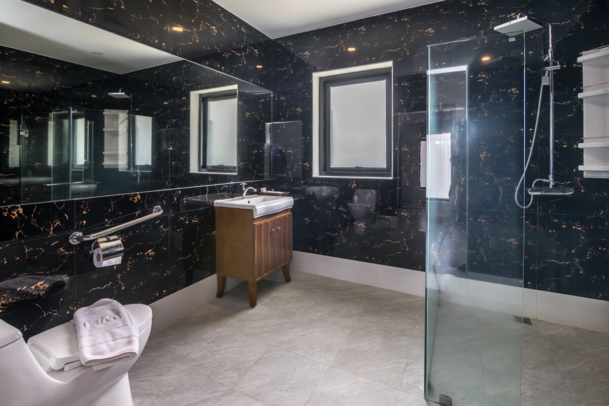 A modern bathroom with a black marble backsplash, a glass shower enclosure, and a wooden vanity.