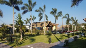 A resort with a thatched-roof building, palm trees, and a pool area. - Tamara Resort Bangsary (Sattahip)