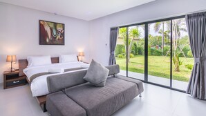 A modern bedroom with a large bed, a sofa, and a view of a lush garden through large windows. - Tamara Resort Bangsary (Sattahip)